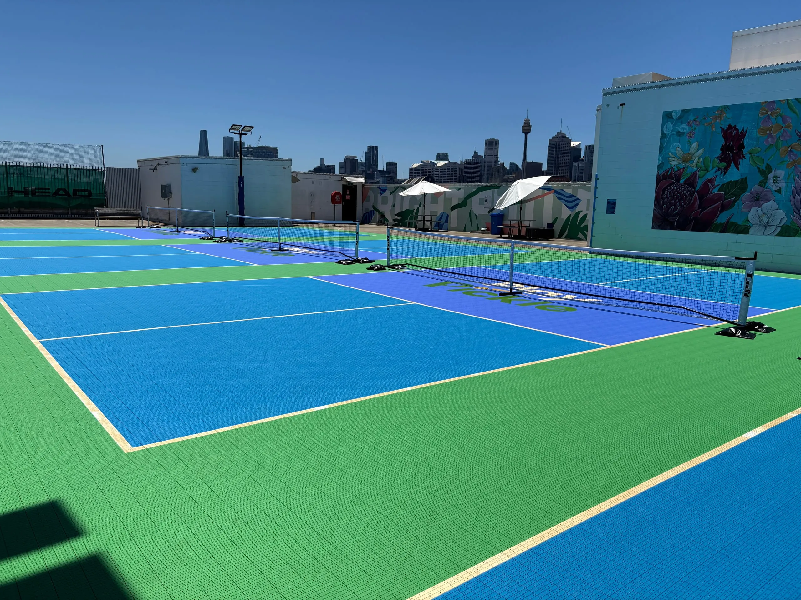 Play Pickle rooftop courts above Broadway Shopping Centre in Ultimo, with the Sydney city skyline and Sydney Tower behind them